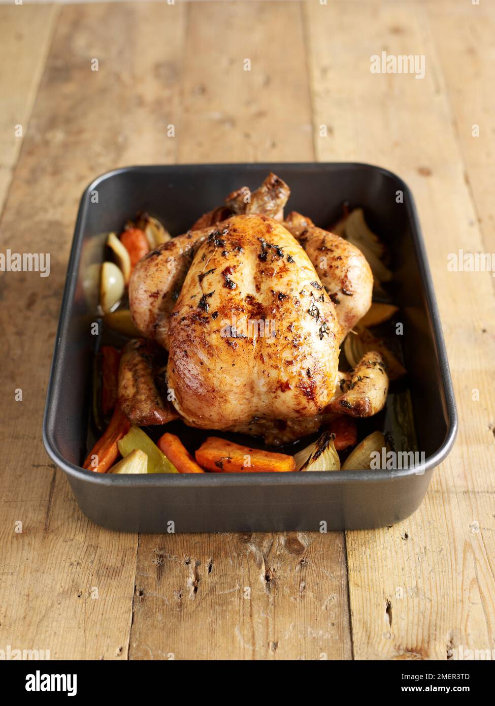 Cooked roast chicken in roasting pan with vegetables, wood background