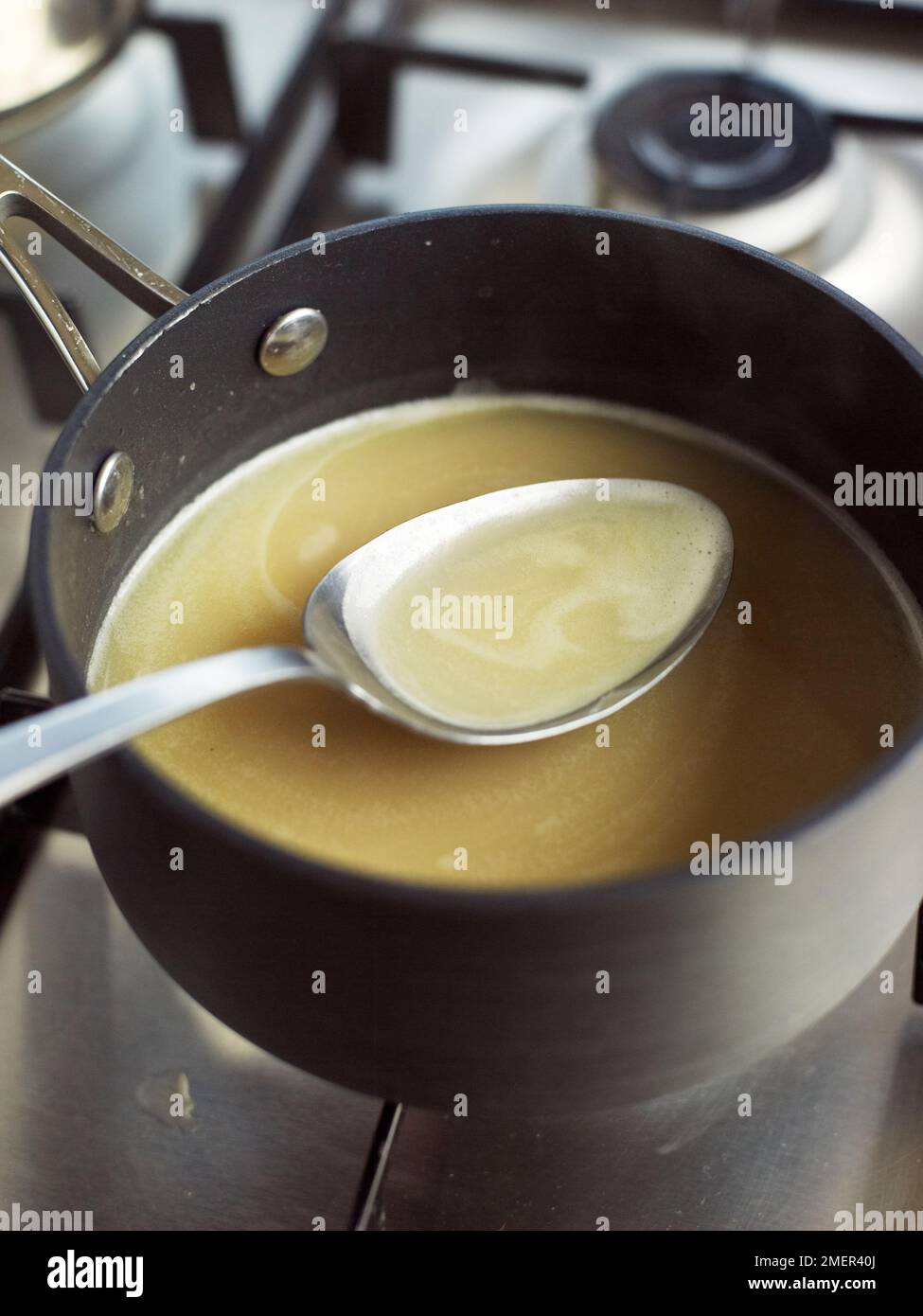 Skimming sauce with spoon to remove scum (making veloute sauce Stock