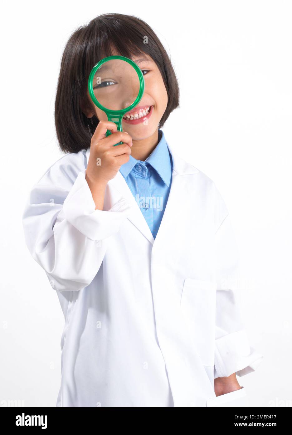 Girl wearing white lab coat, standing holding a magnifying glass to her