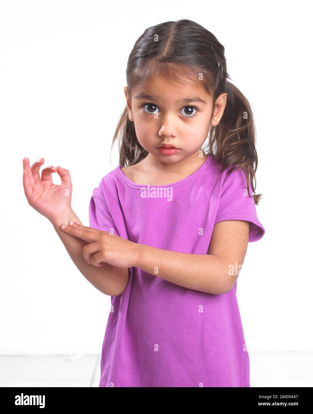 Girl wearing pink top feeling for a pulse in her wrist, 3.5 years Stock Photo