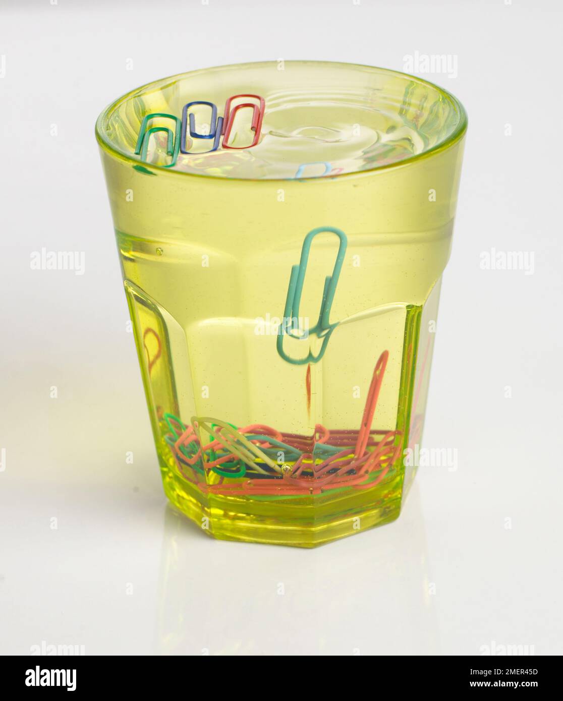 Coloured paperclips in the bottom and floating in full glass of water Stock Photo