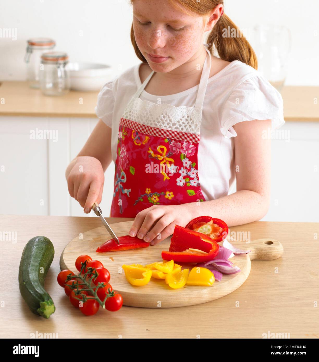 Girl chopping courgette, peppers and tomatoes, 9 years Stock Photo