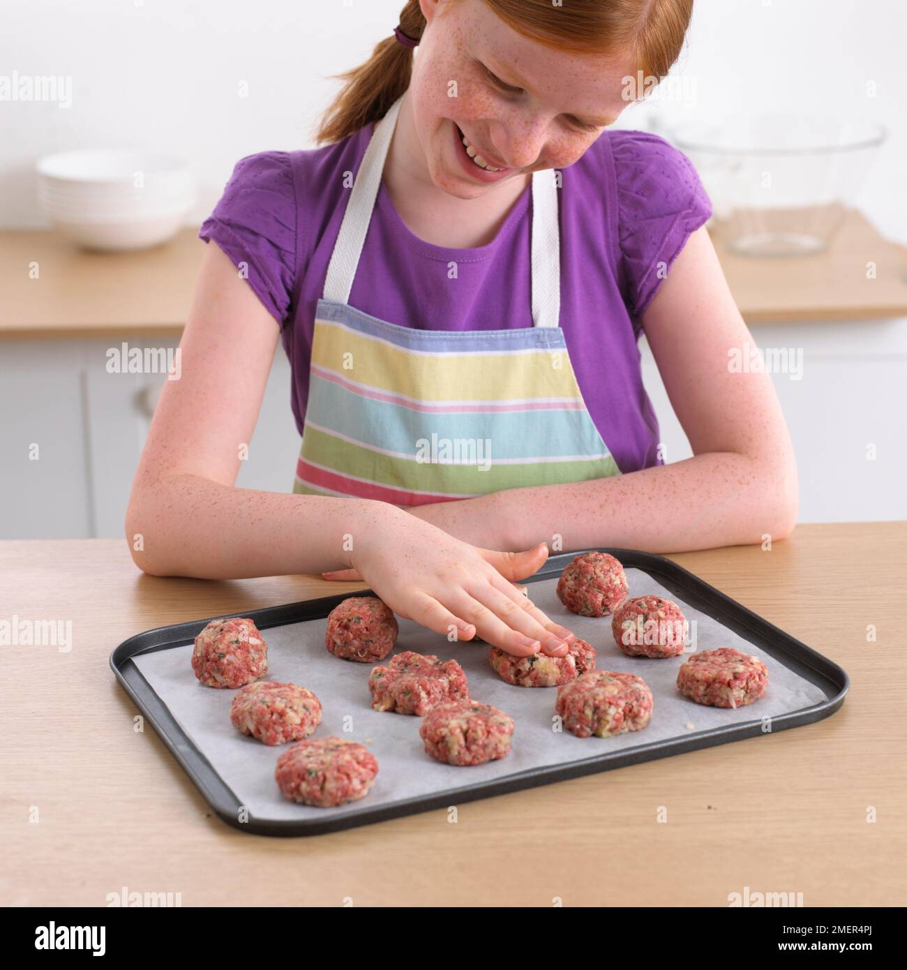 Girl molding mini burgers with minced beef on a baking tray, 9 years