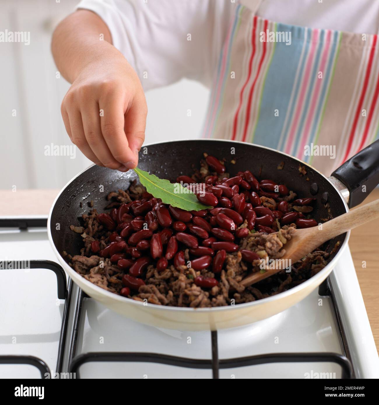 Adding bay leaf to pan of fried minced beef and red kidney beans Stock