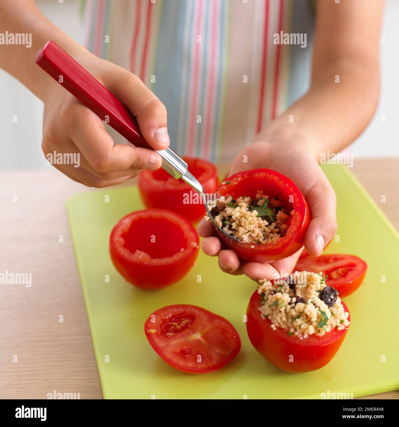 Filling hollowed out large tomatoes with cous cous, raisin and herb salad Stock Photo