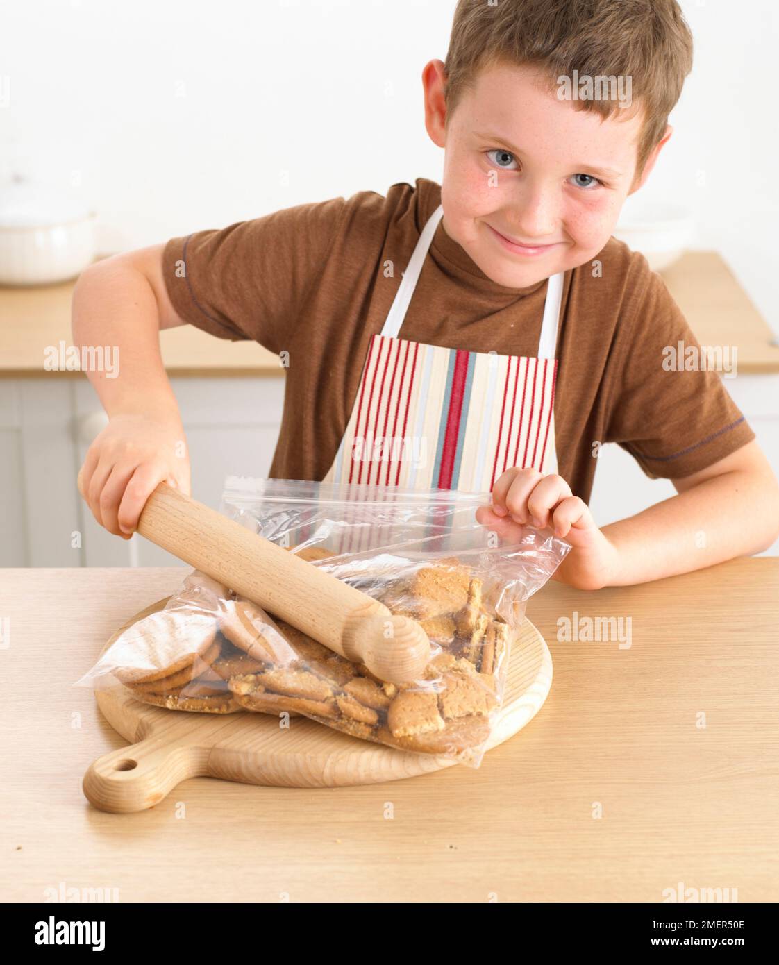 Boy crushing biscuits in a bag using a rolling pin, 8 years Stock Photo