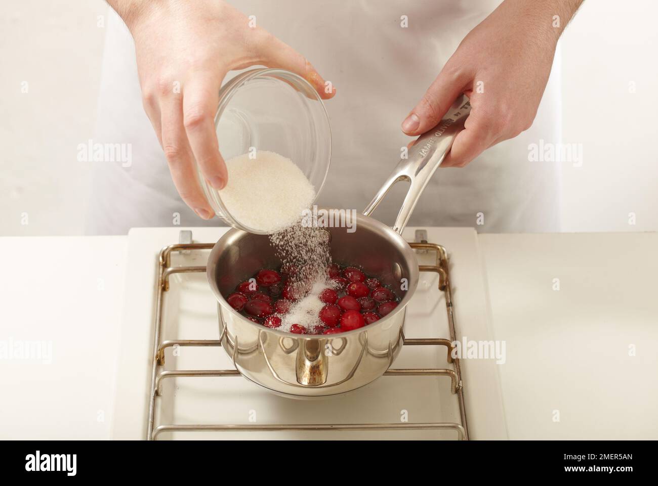 Adding sugar to saucepan of cranberries Stock Photo