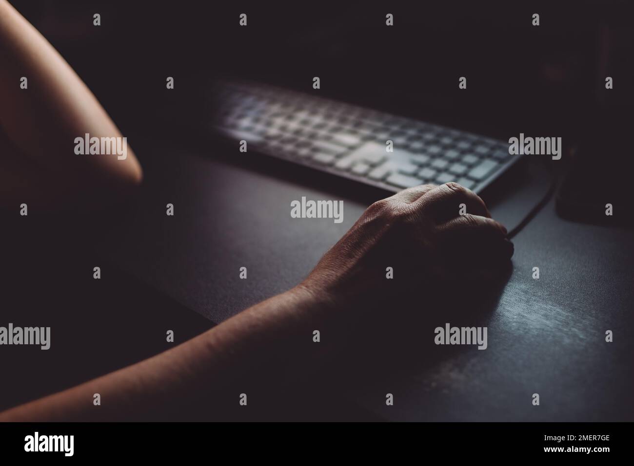 Woman using desktop computer mouse in dark home office interior, closeup of hands with selective focus Stock Photo