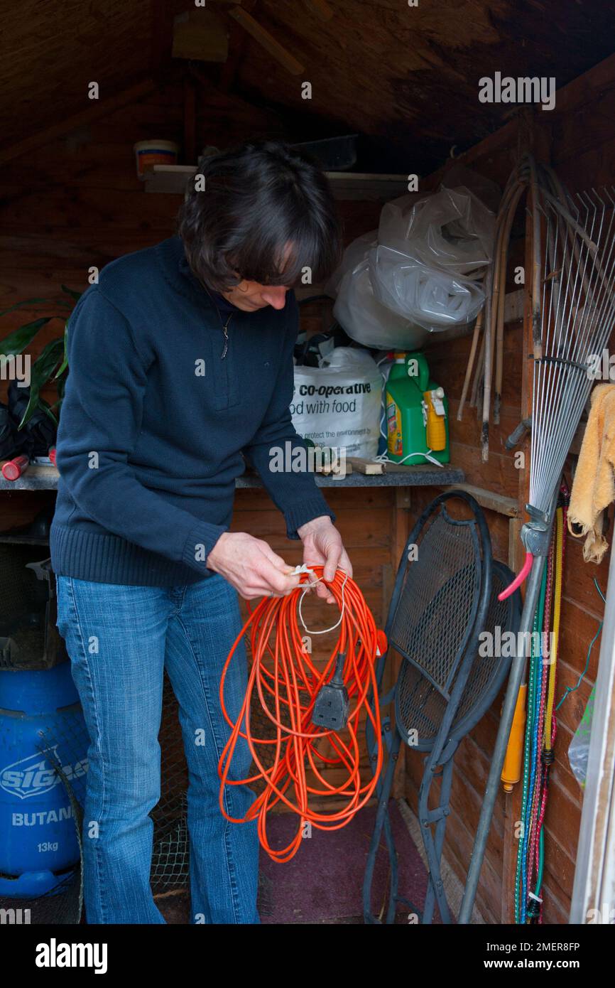 Tidying up garden shed winding up extension lead Stock Photo Alamy