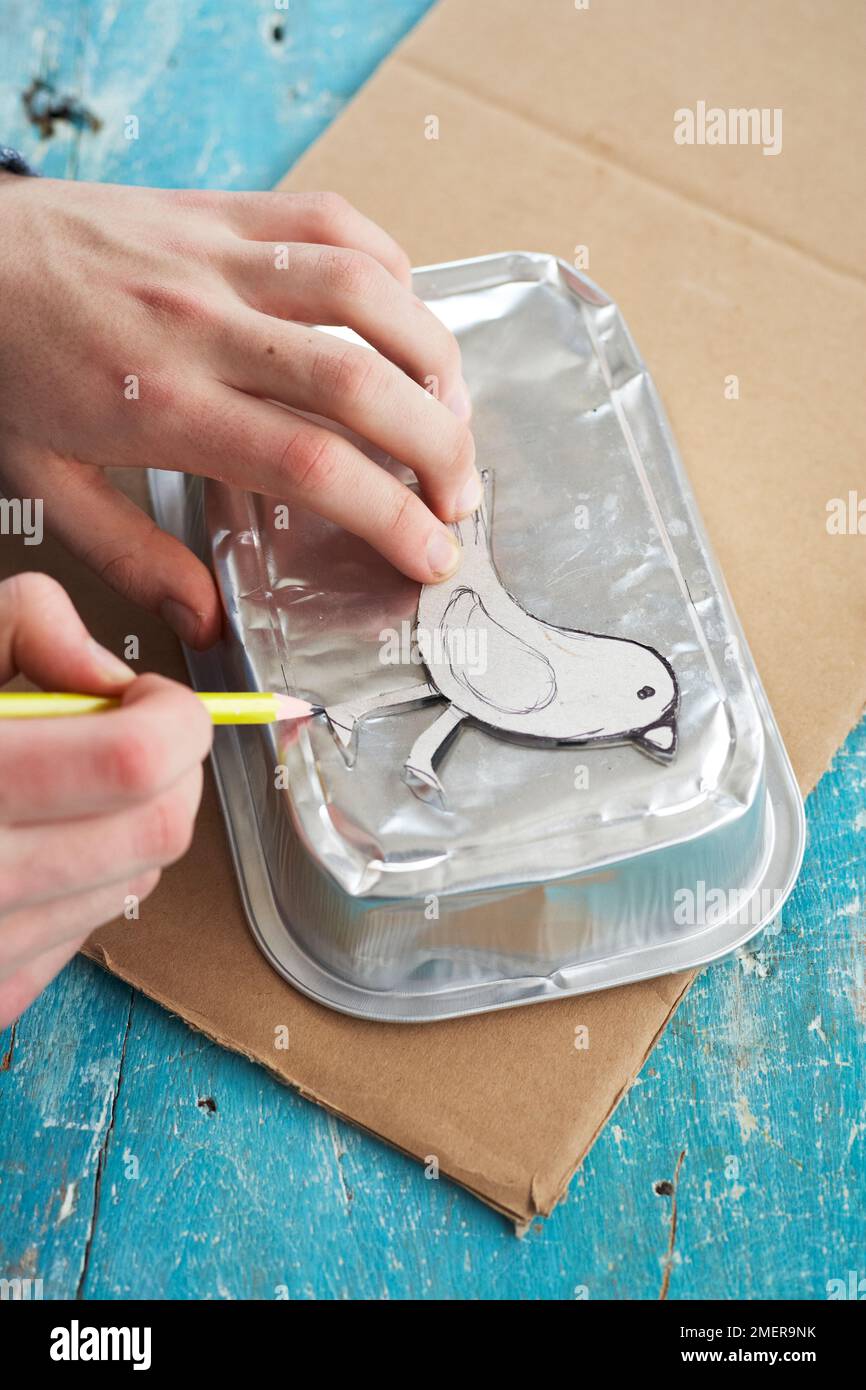 Drawing bird shape onto metal foil takeaway container, making paper birdcage Stock Photo