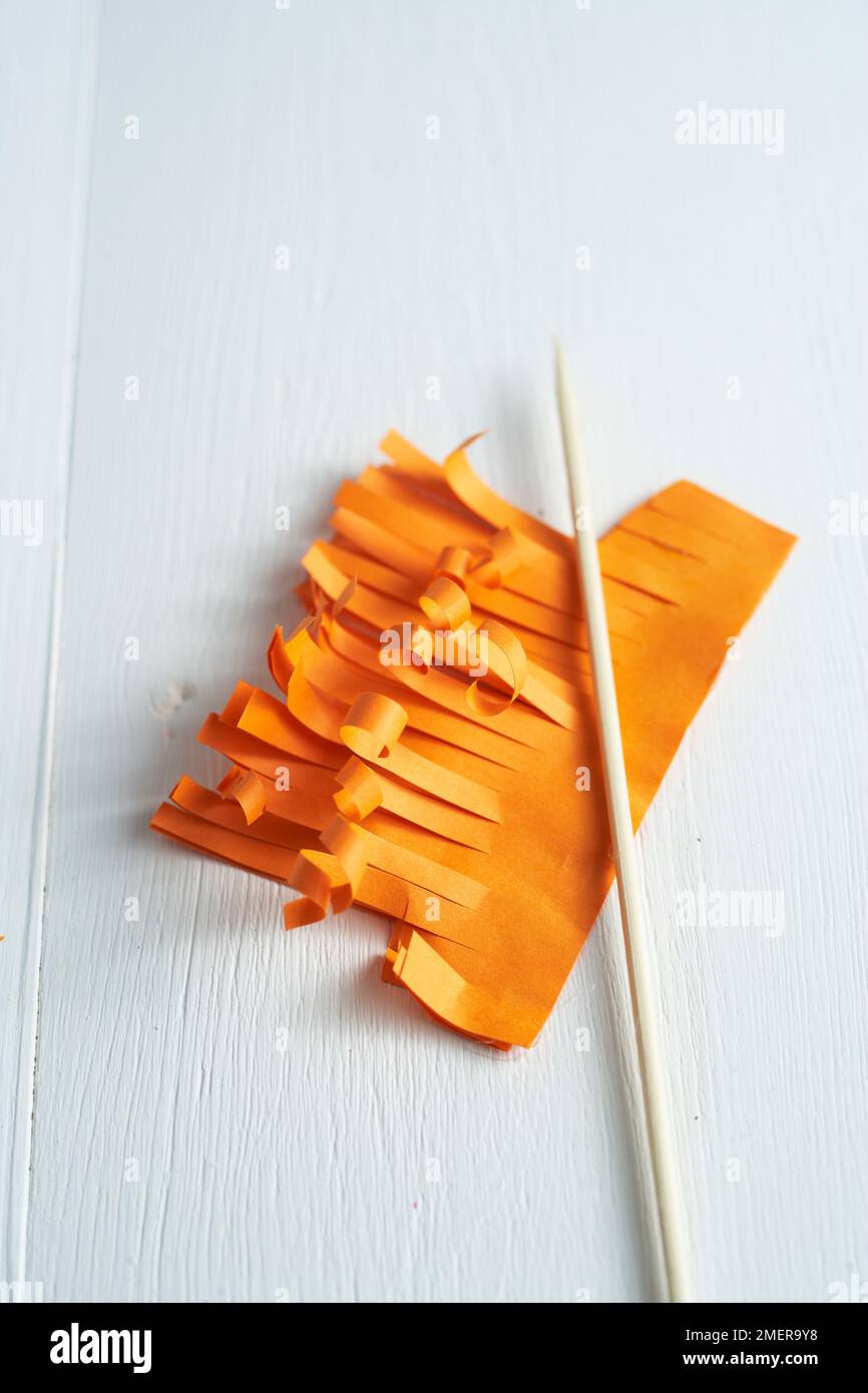 Cutting strands into folded orange paper, making hair for paper fairy Stock Photo