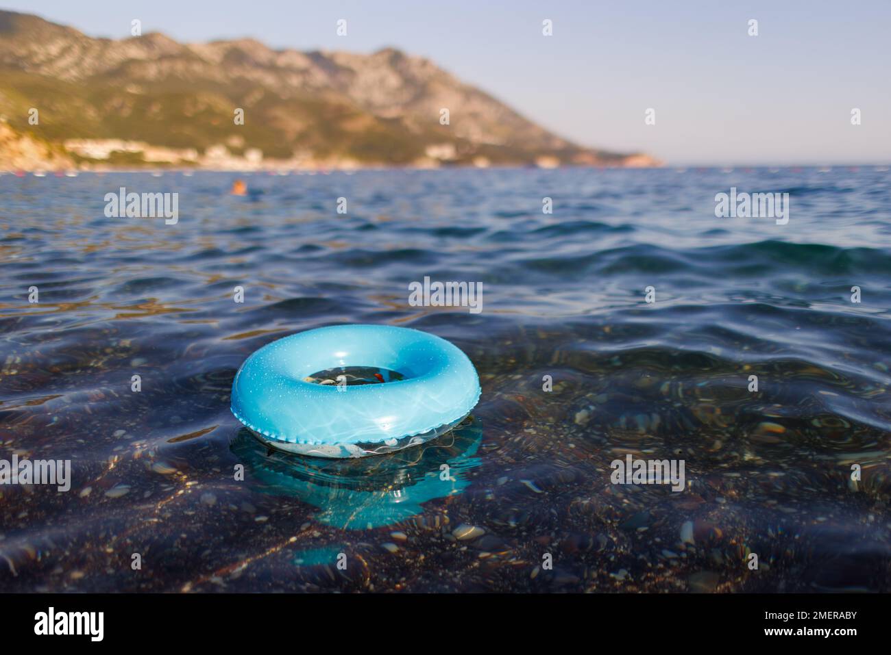 A small bright lost inflatable ring of blue color floats alone in the empty transparent blue Adriatic Sea in the evening Stock Photo