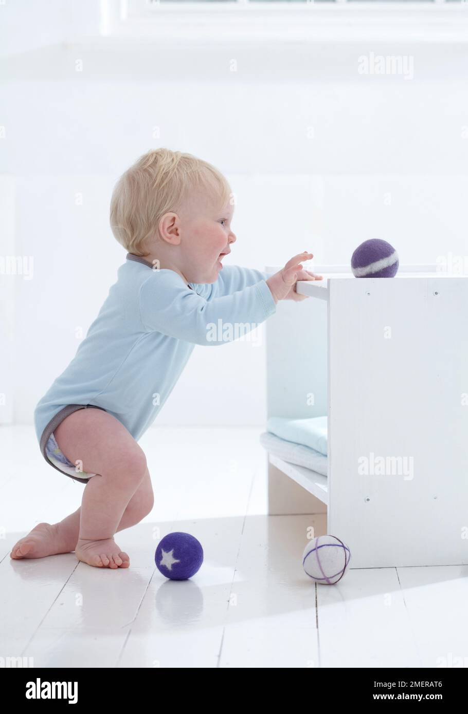 Boy pulling himself up on 12 months, reaching for felt ball