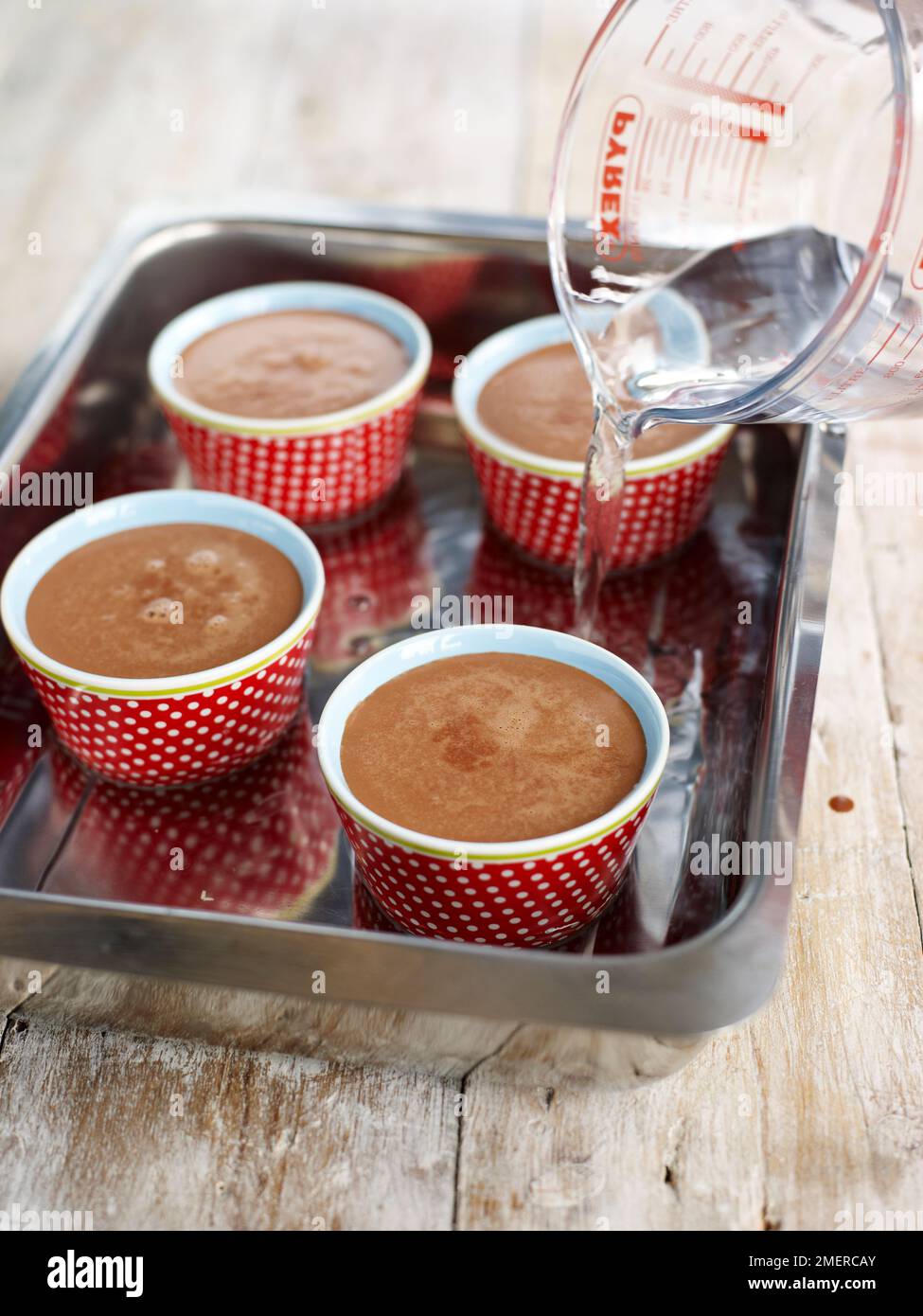 Chocolate pot desserts in ramekins in roasting tin, hot water being poured into tin, ready to be baked in the oven Stock Photo