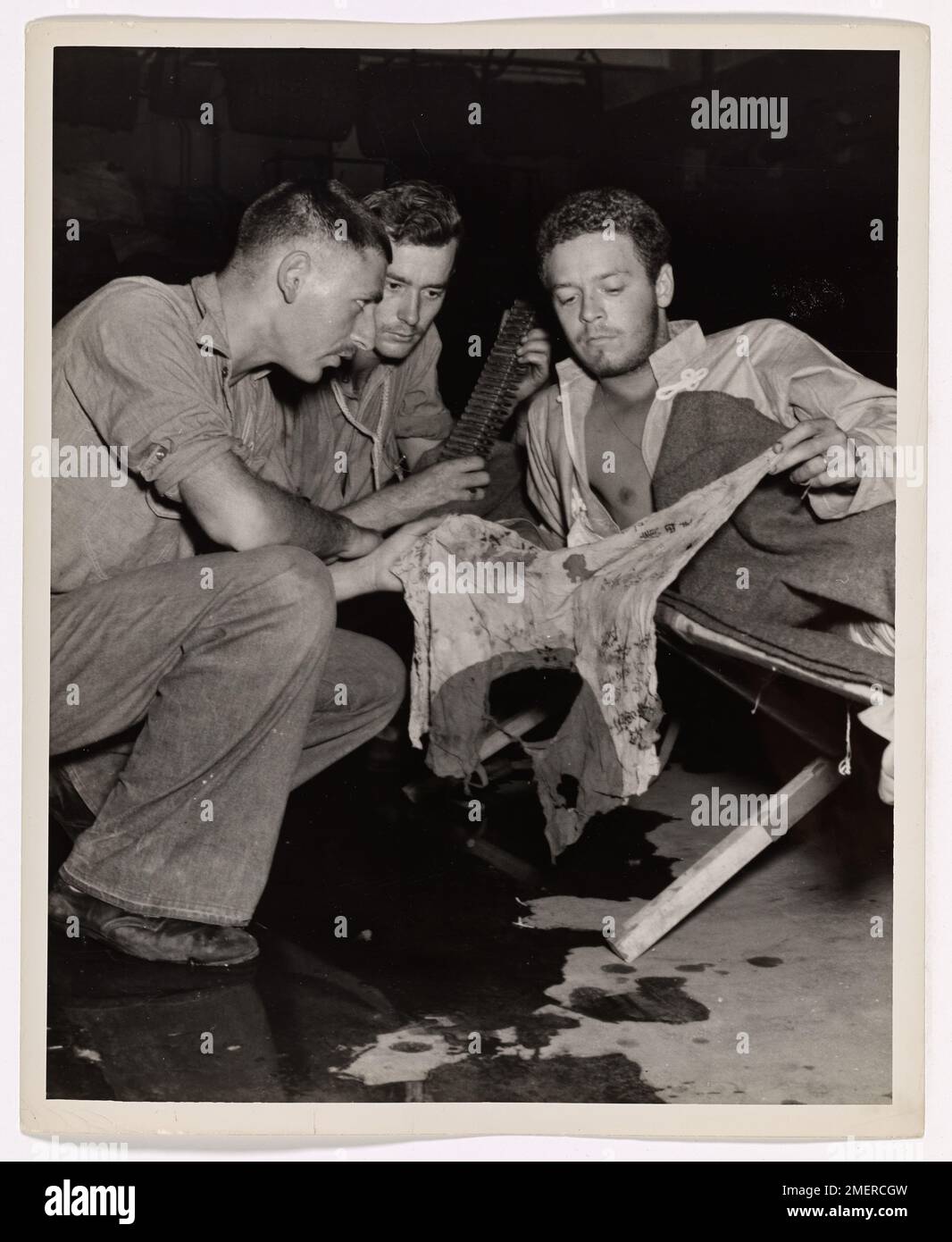 The Coast Guard Brings Out the Wounded. Pharmacist's Mate on the job -- Aboard a Coast Guard-manned LST somewhere in the Pacific invasion zone, Marine Corp. John T. Curry (right) of Decatur, Illinois, wounded in a beach assault, exhibits a bullet-riddled Jap battle flag to two Coast Guardsmen on duty in the floating hospital. They are David Green (foreground), pharmacist's mate second class, of Staten Island, N.Y. and Shelby K. Lay, boatswain's mate second class, of Harrison, Arkansas. Stock Photo