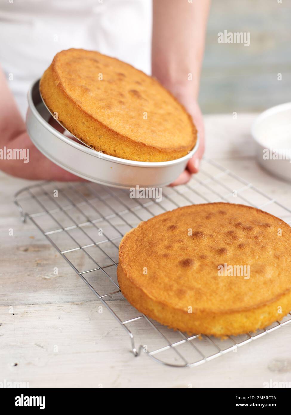 Lifting out sponge cake from tin while second sponge cake cools on rack