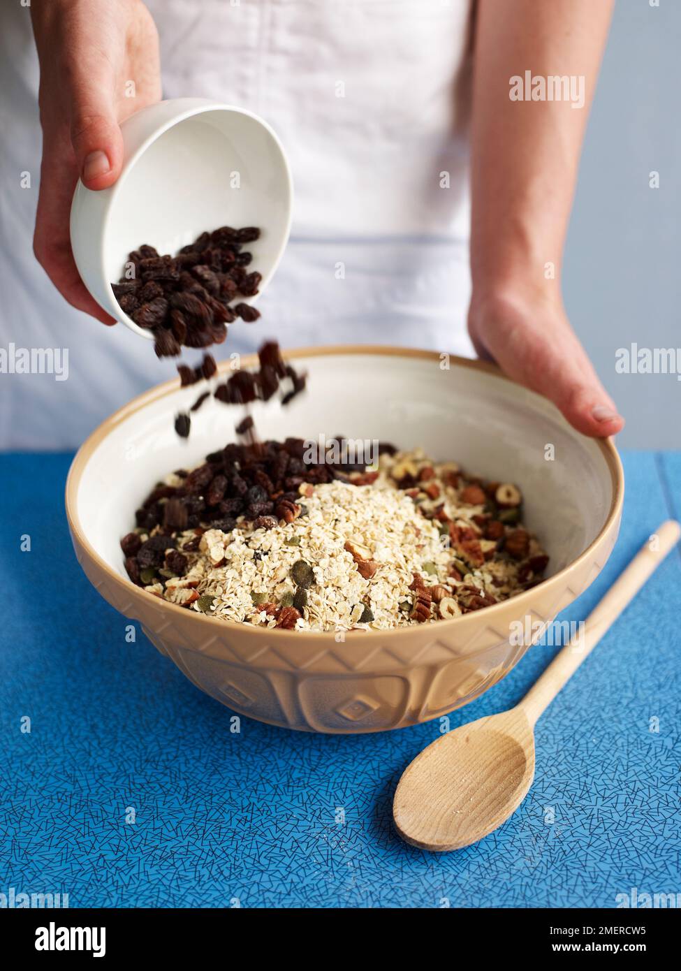 Pouring raisins into a large mixing bowl of brown sugar, rolled oats