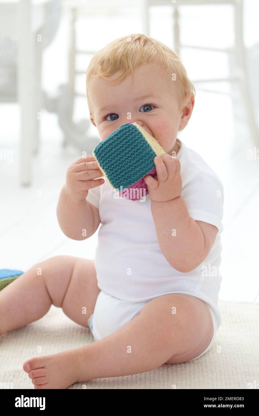 Baby boy chewing knitted building block, 10 months Stock Photo