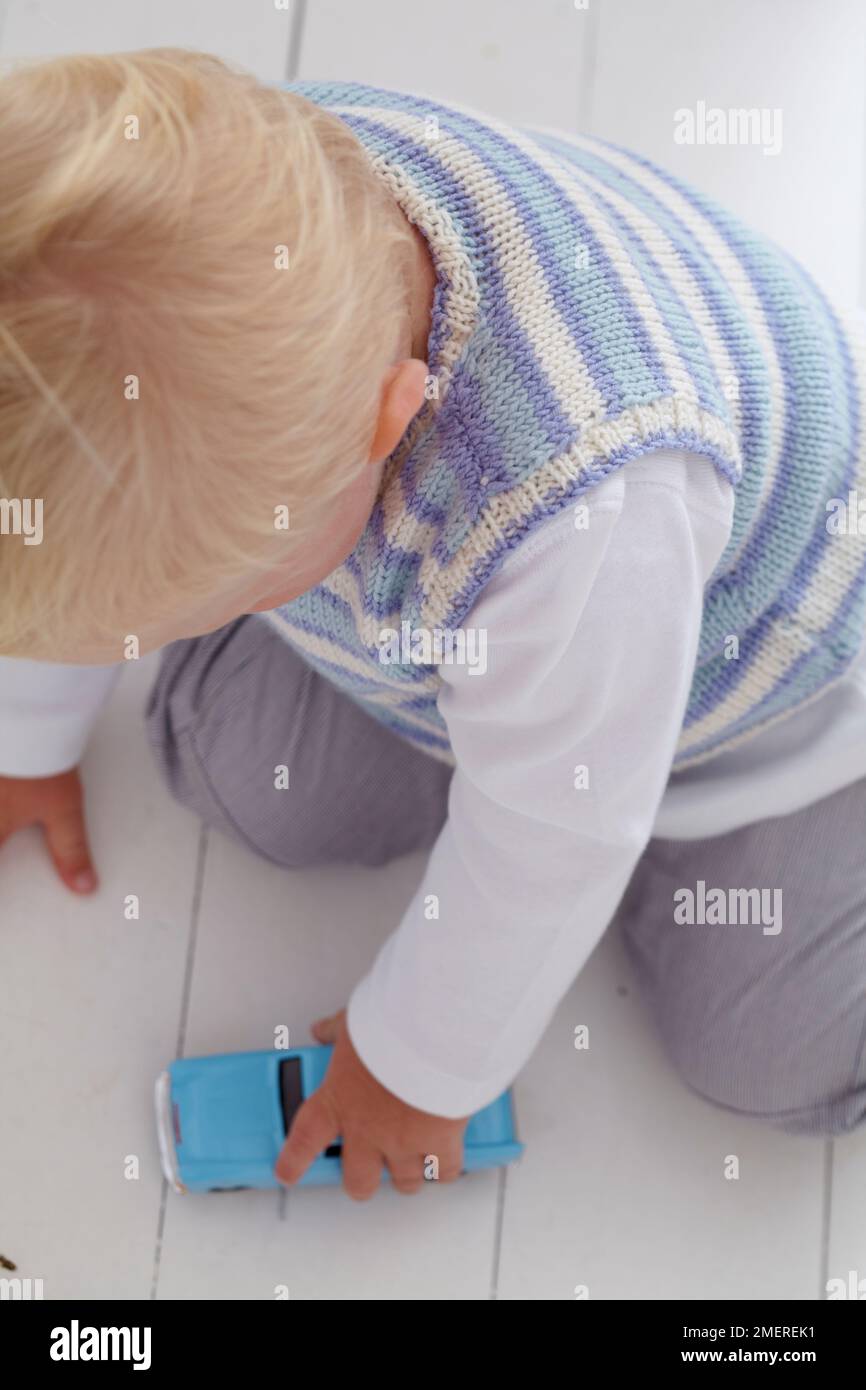 Baby boy sitting on floor playing with blue car, 14 months Stock Photo