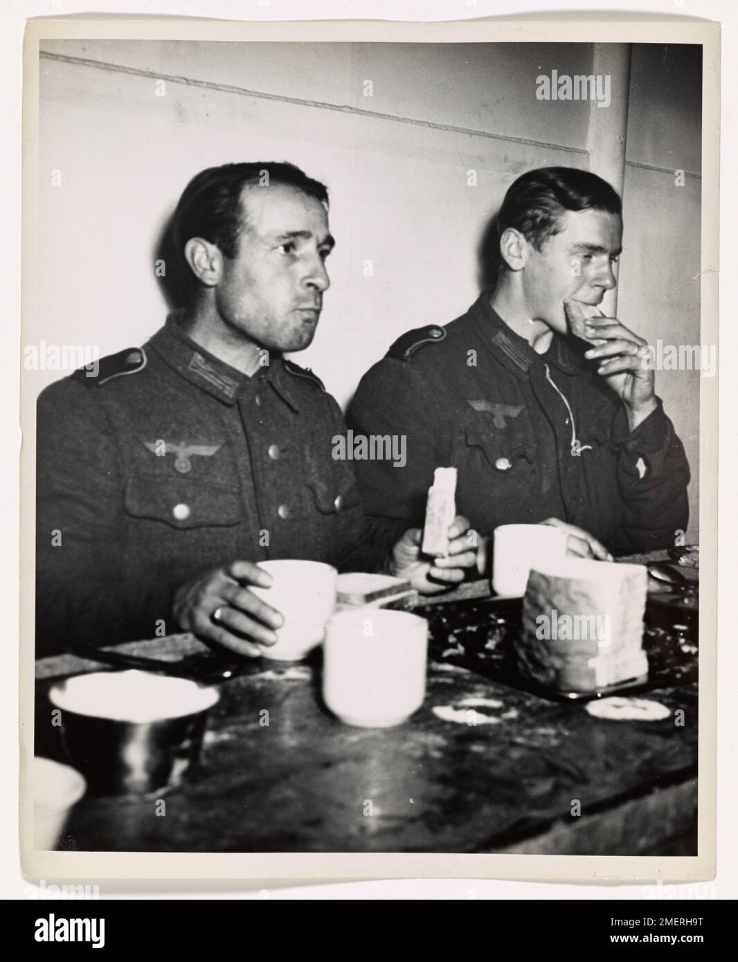 Photograph of Two Nazi Prisoners Aboard a Coast Guard-manned Troop Transport Headed for the United States. The Awakening. Aboard a Coast Guard-manned troop transport headed for the United States, two Nazi prisoners present a picture of downcast disillusion as they hungrily munch the first white bread they have tasted in many months. Captured in the irresistible Yankee push from the Normandy beaches toward Cherbourg, these ex-'supermen' have been rudely awakened from mad Hitlerite dreams of world conquest. The first shipment of hundreds of Nazis captured in France has arrived at an Atlantic por Stock Photo
