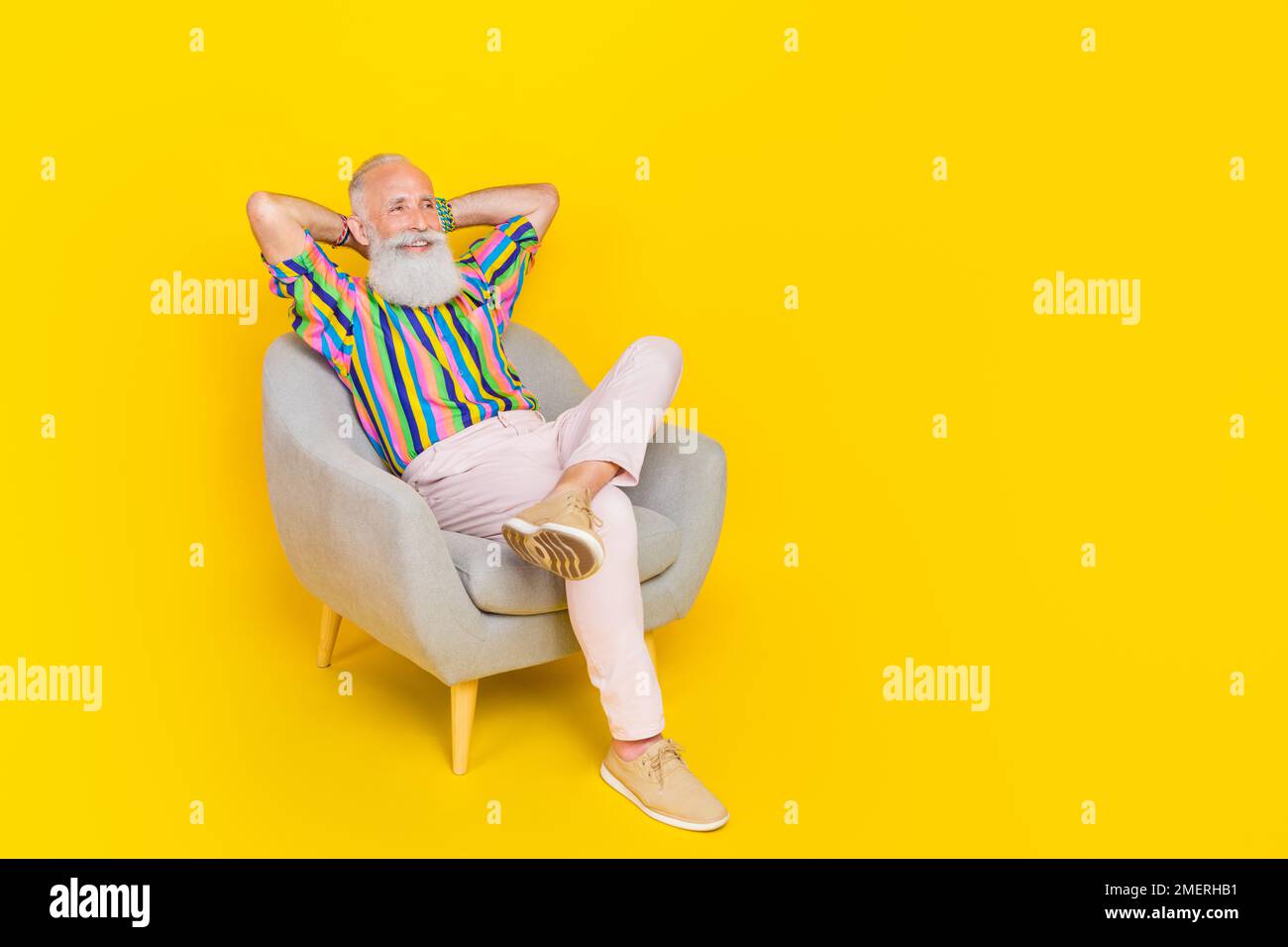 Full length photo of cheerful positive man sit chair arms behind head look empty space isolated on yellow color background Stock Photo