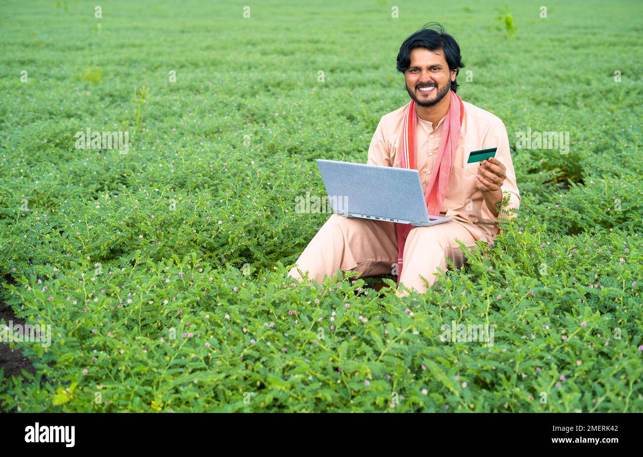 wide shot of Young farmer at field making online payment using credit card on laptop - concept of modern farming, online banking service and wireless Stock Photo