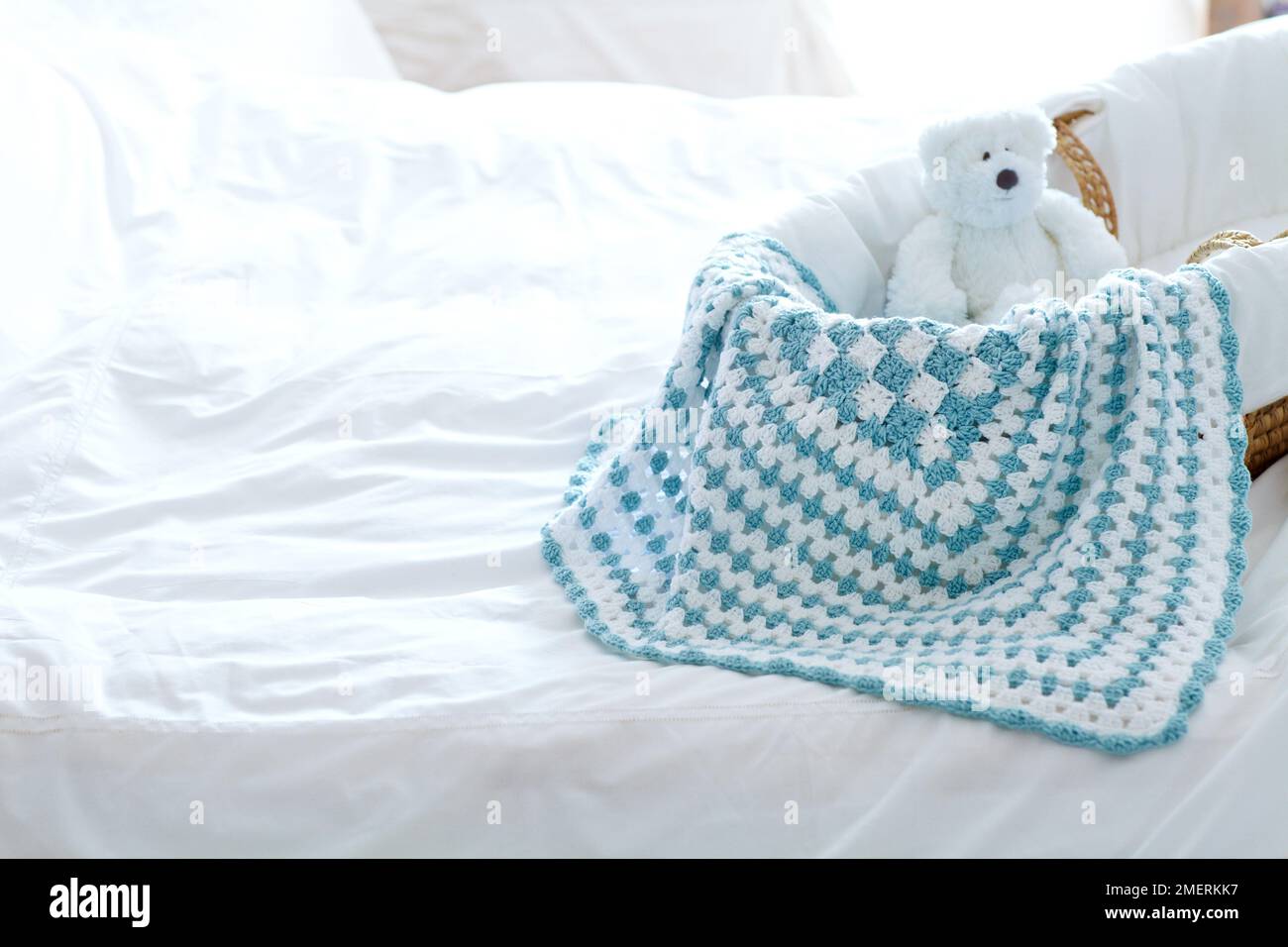 Crocheted baby blanket and teddy in moses basket on bed Stock Photo Alamy