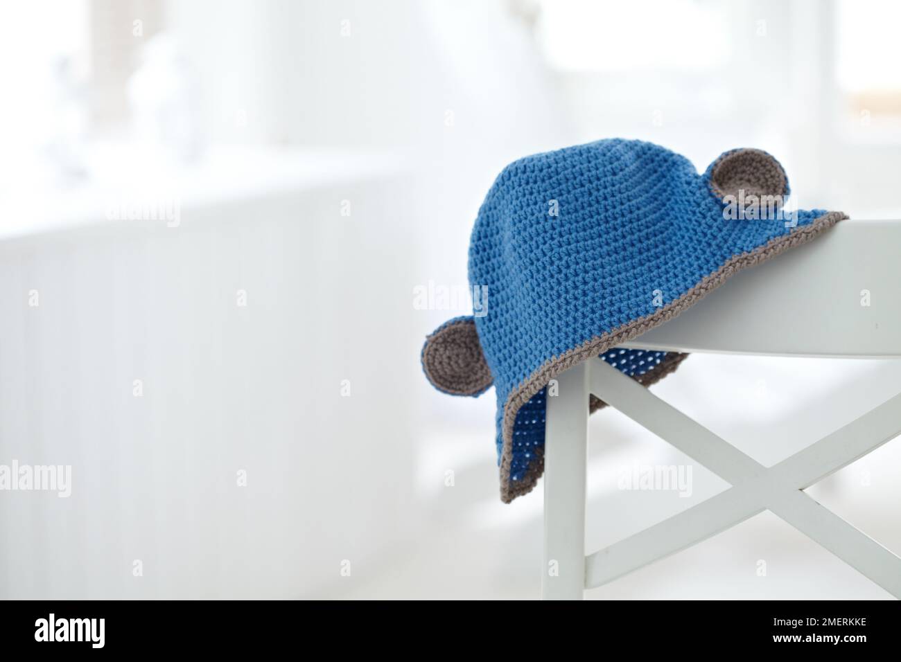 Crocheted baby's hat with 'ears' over edge of chair Stock Photo