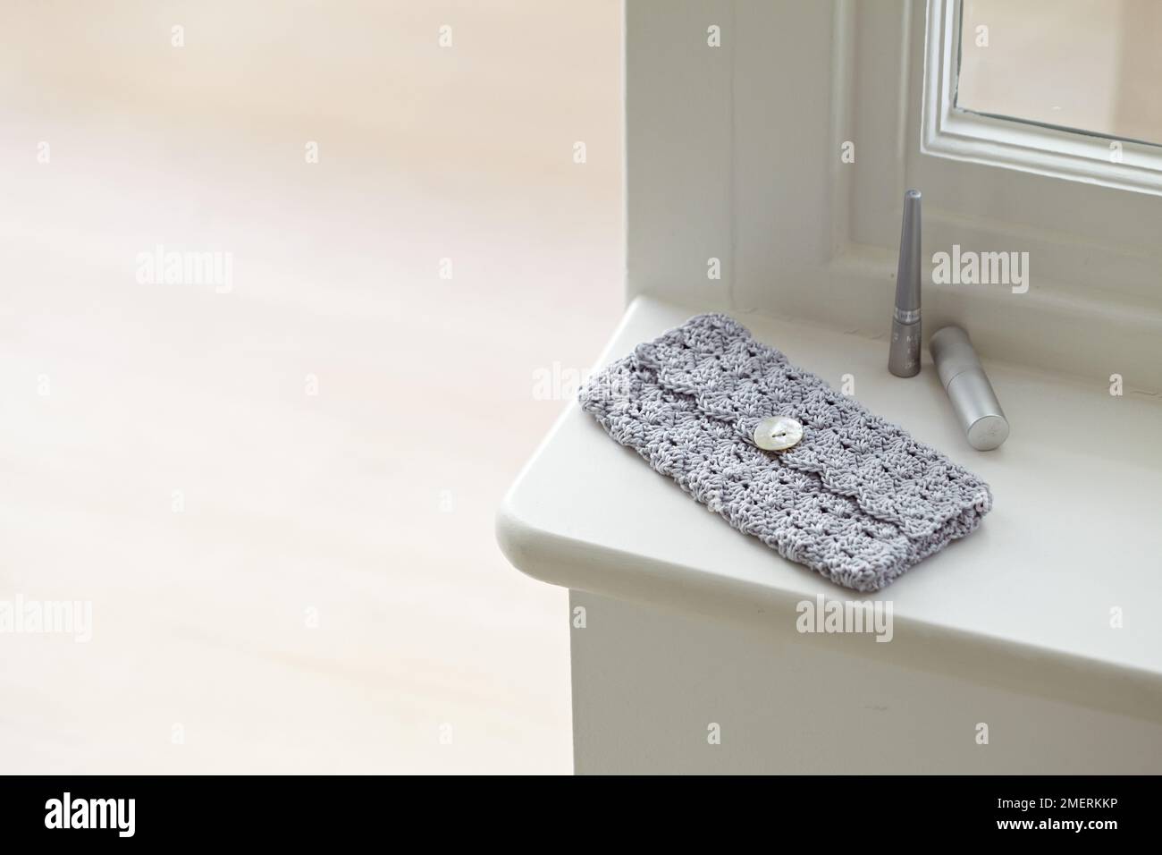 Clutch bag crocheted in cluster and shell stitch pattern, and lipsticks on window sill Stock Photo