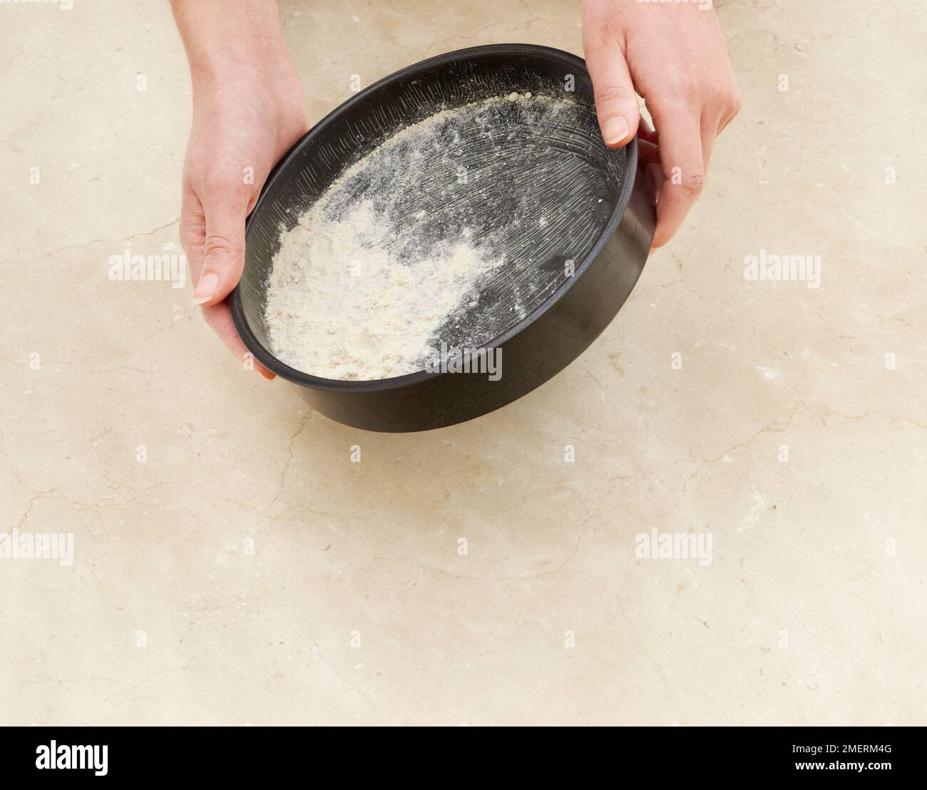 Dusting a greased cake tin with flower Stock Photo