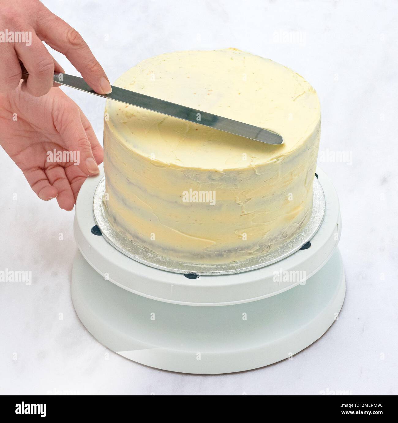 Spreading crumb coat of icing on cake Stock Photo Alamy