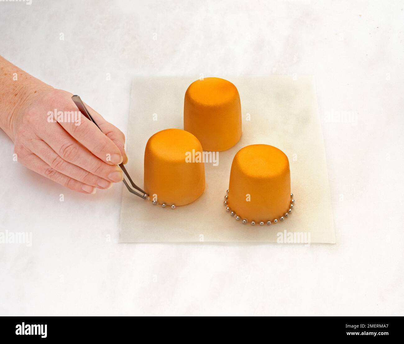 Sticking small silver edible balls at the bottom of three small cakes
