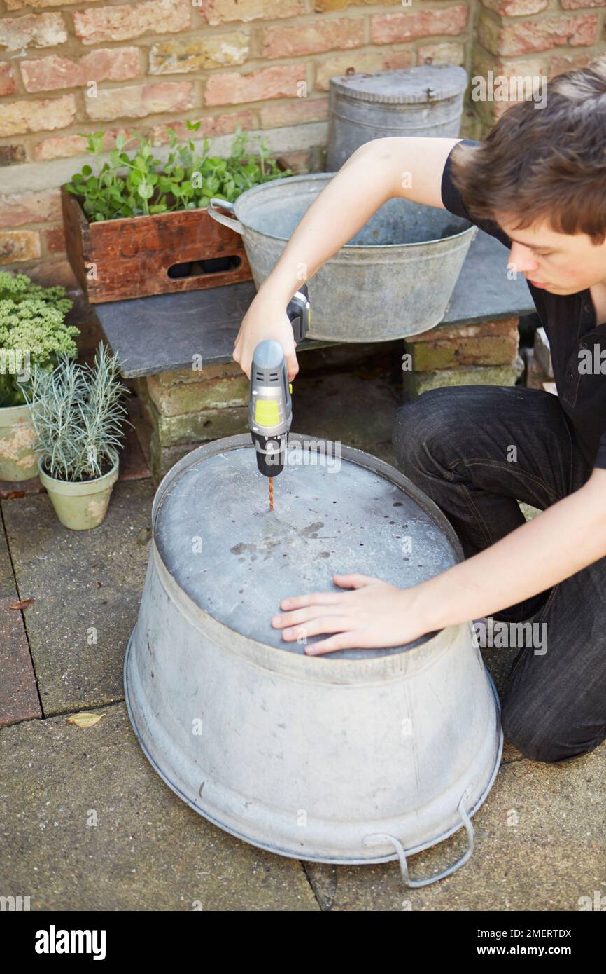 Drilling holes in bottom of a vintage galvanized steel bath Stock Photo