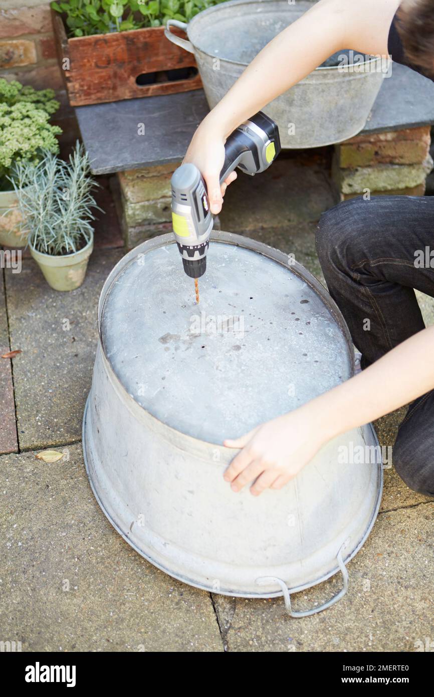 Drilling holes in bottom of a vintage galvanized steel bath Stock Photo