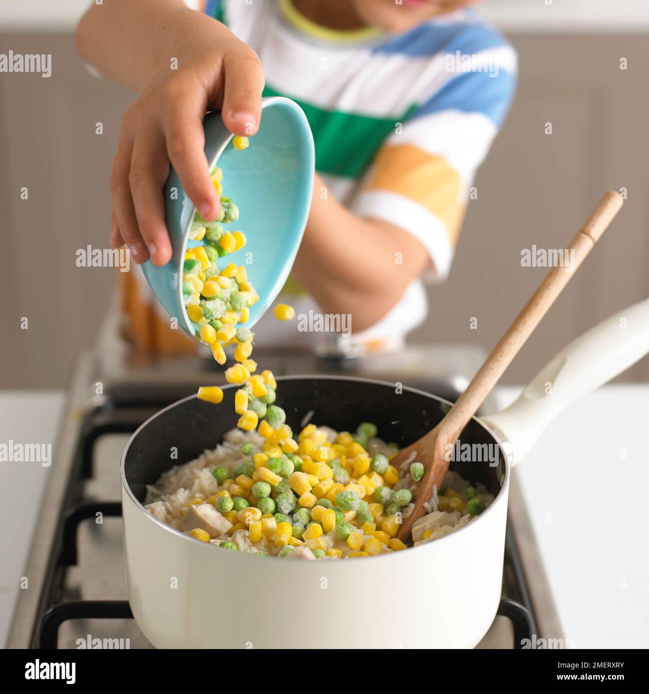Making chicken risotto, Pouring peas and sweetcorn into saucepan of