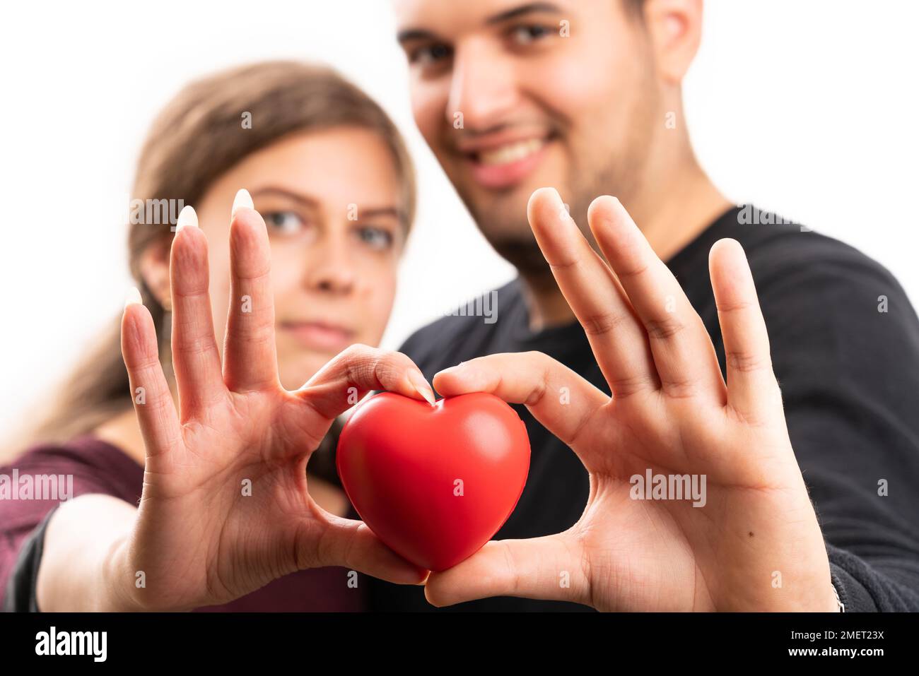 Close-up with selective focus of red heart held presented by cute girlfriend and boyfriend couple as romantic love concept isolated on white studio ba Stock Photo