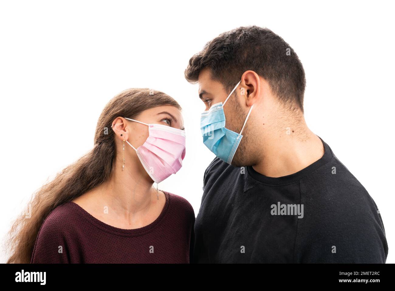 Girlfriend wearing pink disposable medical or surgical mask as sars covid19 influneza prevention looking at cute boyfriend with blue protective face c Stock Photo