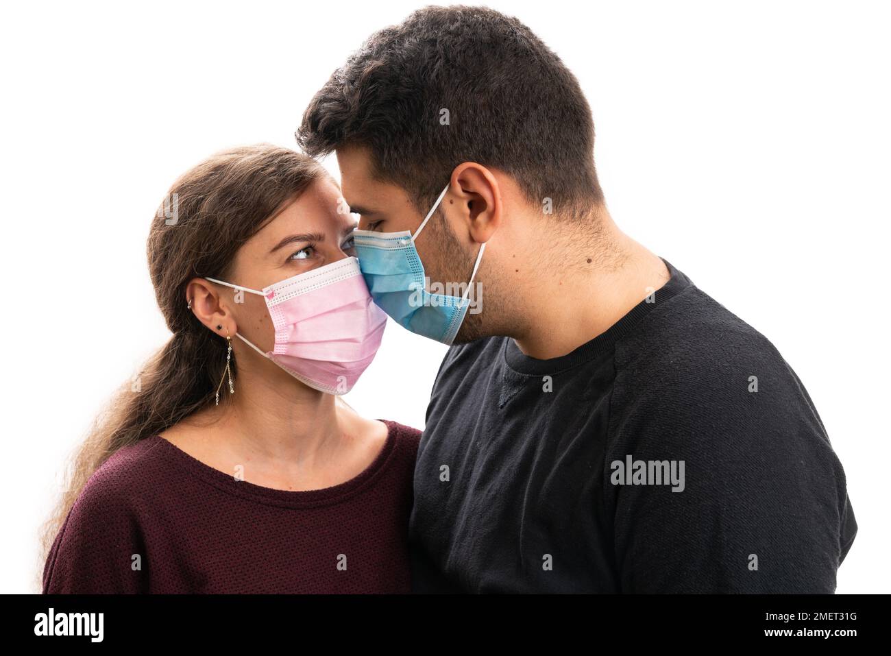 Adult woman and man couple wearing medical or surgical mask pink blue touching nose as eskimo kiss loving isolated on white studio background Stock Photo