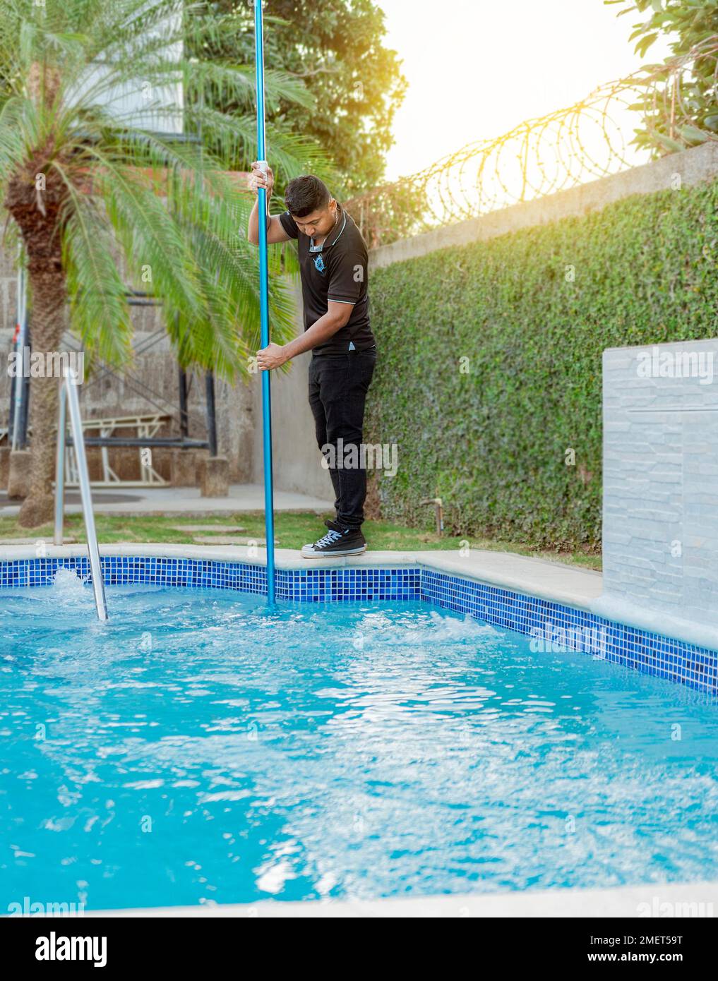 Young man cleaning a swimming pool with a vacuum hose, Maintenance