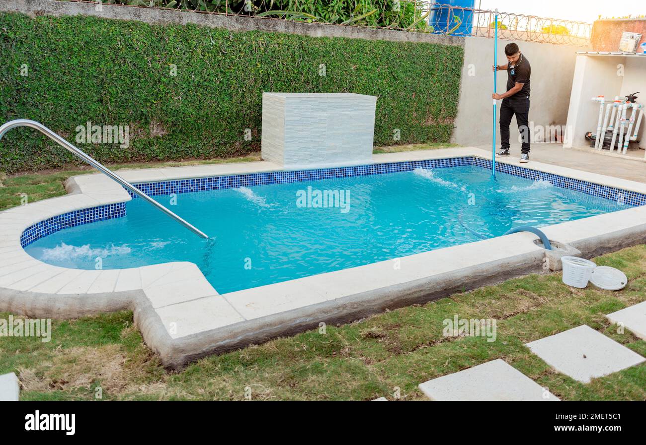 Maintenance person cleaning pool with vacuum hose. Man cleaning and