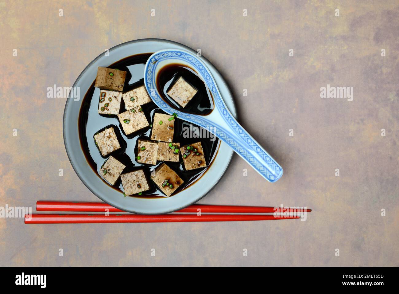 Soy sauce marinated tofu cubes in bowl with Asian ceramic spoon and
