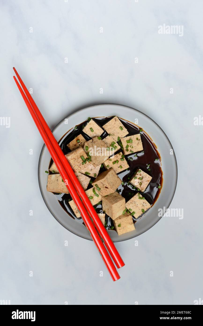 Soy sauce marinated tofu cubes in bowl with Asian chopstick Stock Photo