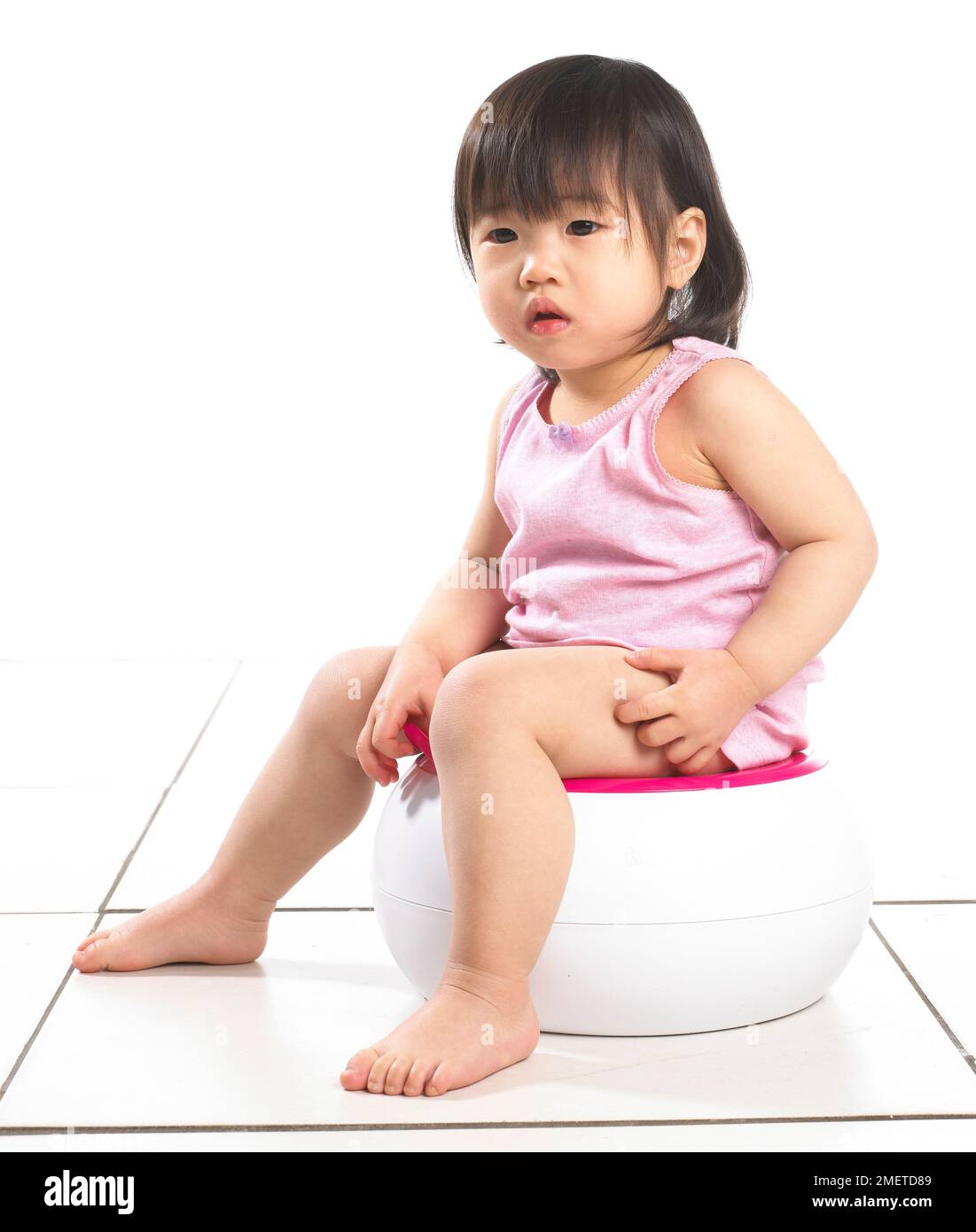 Girl wearing pink vest sitting on a white potty, 20 months Stock Photo