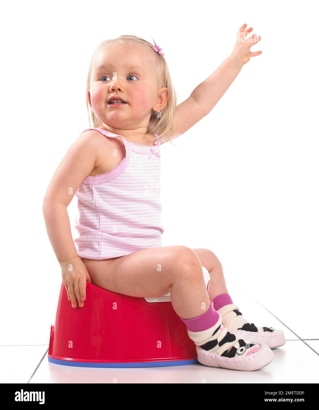 Girl wearing vest and slippers sitting on a red potty, 20 months Stock