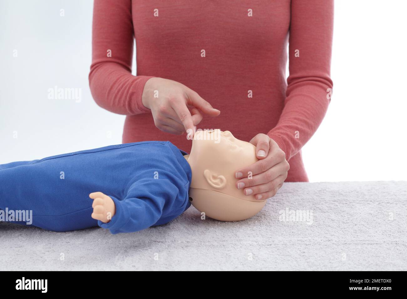 First aid medical checks and treatment of unconscious infant, using dummy, making sure that airway is still open by keeping one hand on forehead and fingertip of other hand under tip of infant's chin, giving CPR Stock Photo