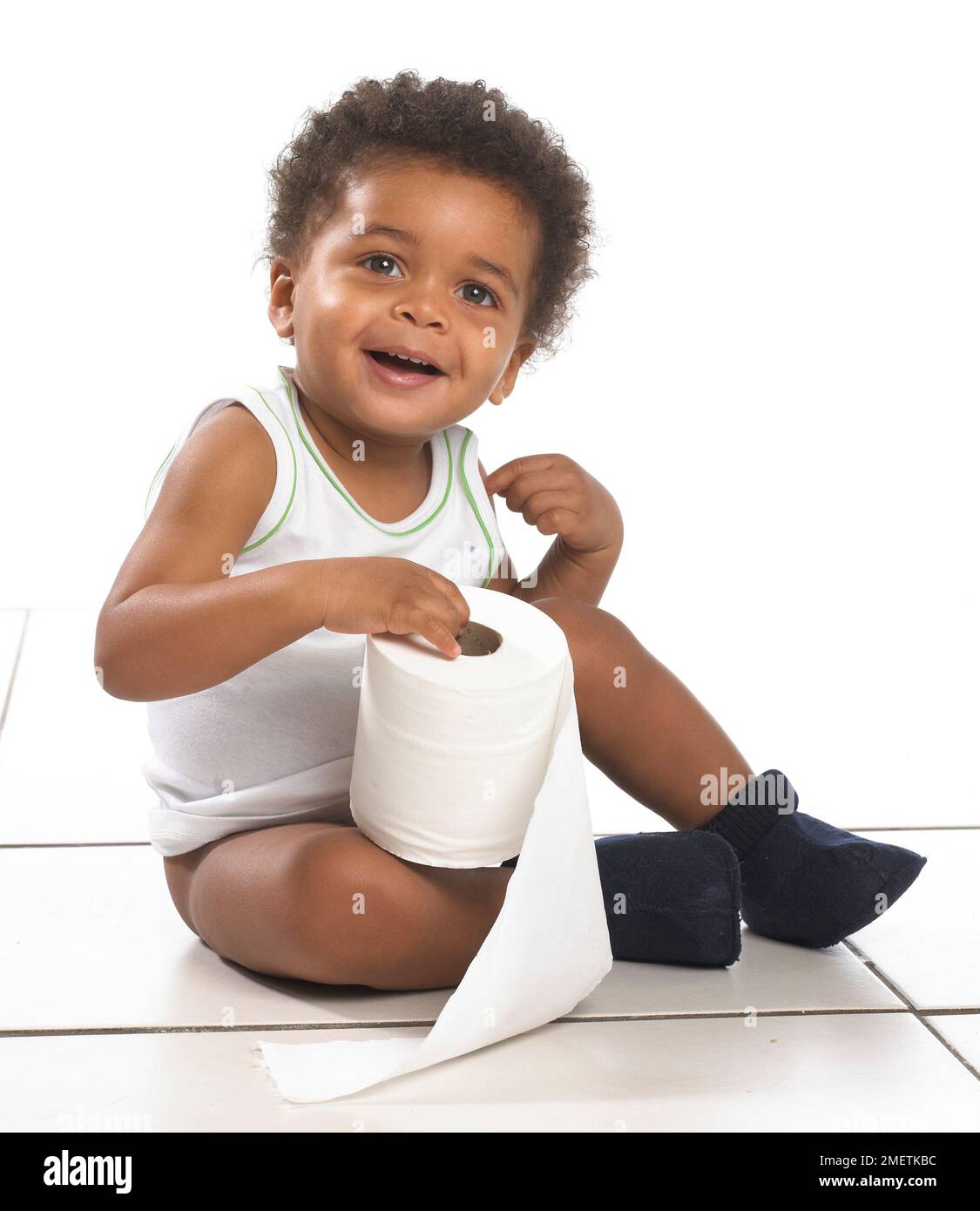Boy wearing vest and slippers sitting on floor holding roll of toilet