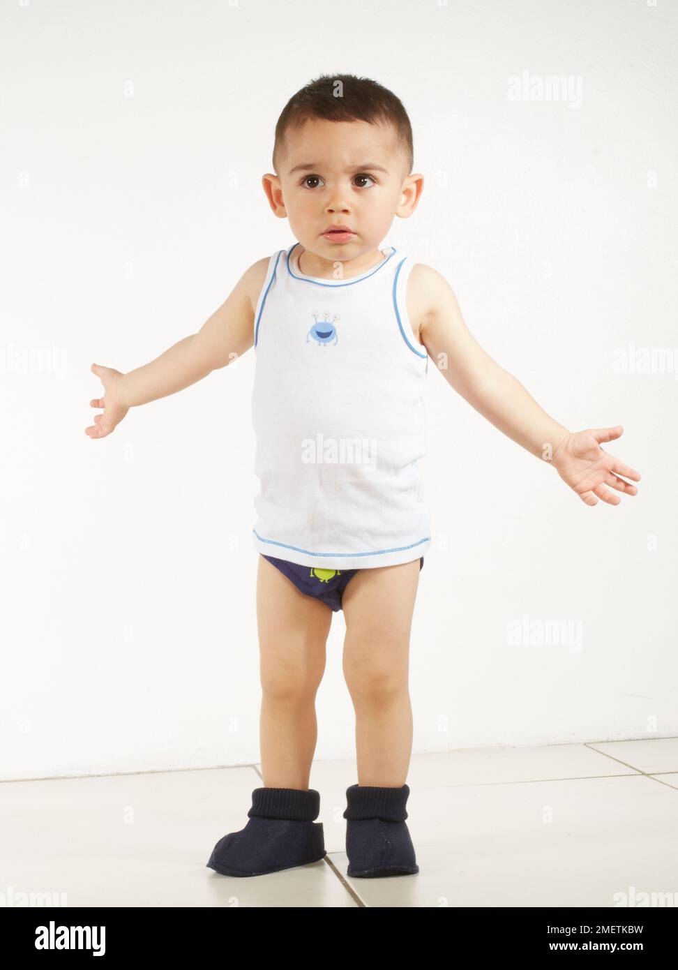 Boy wearing vest, pants and slippers with arms outstretched, 15 months Stock Photo