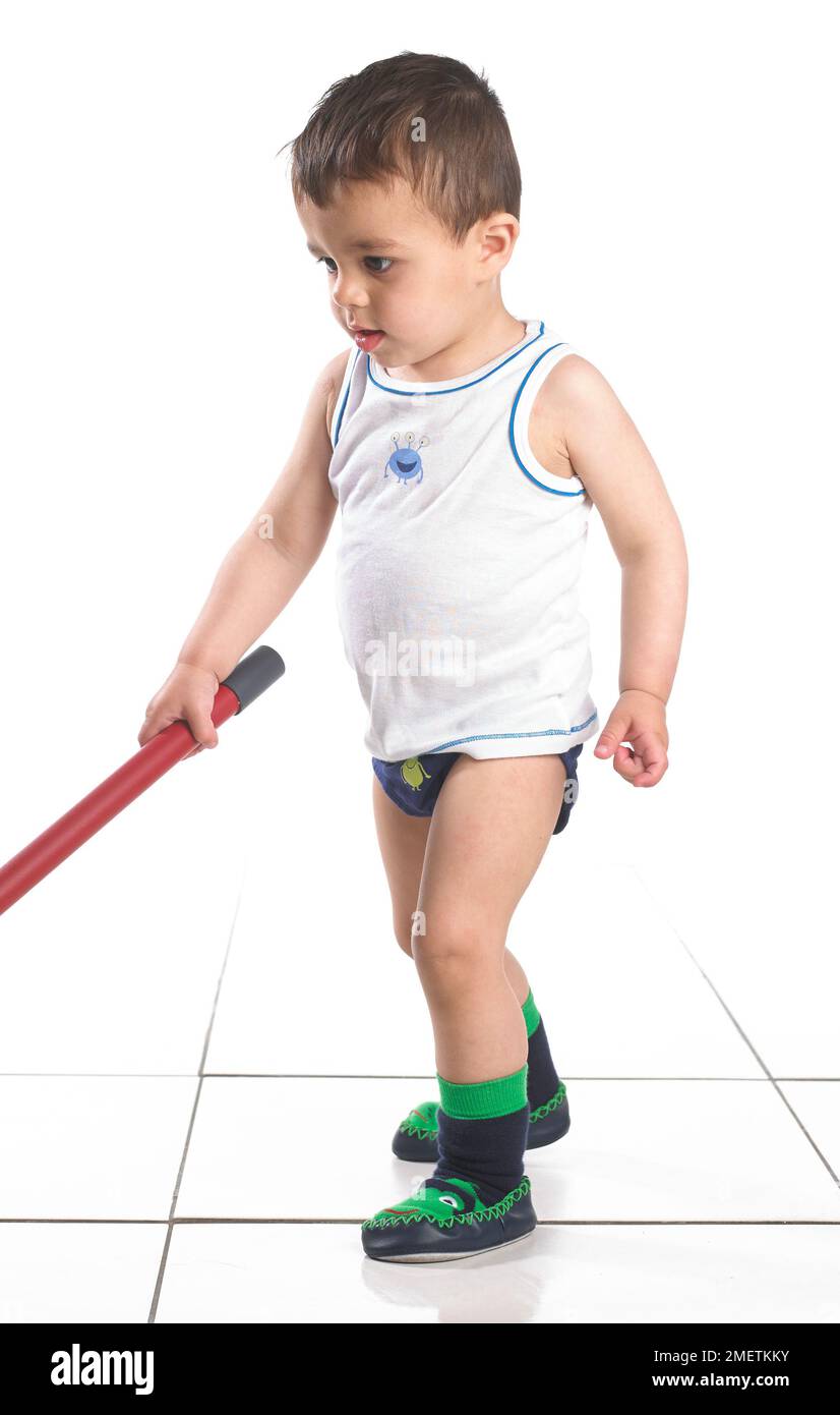 Boy wearing vest and slippers playing with a mop, 15 months Stock Photo