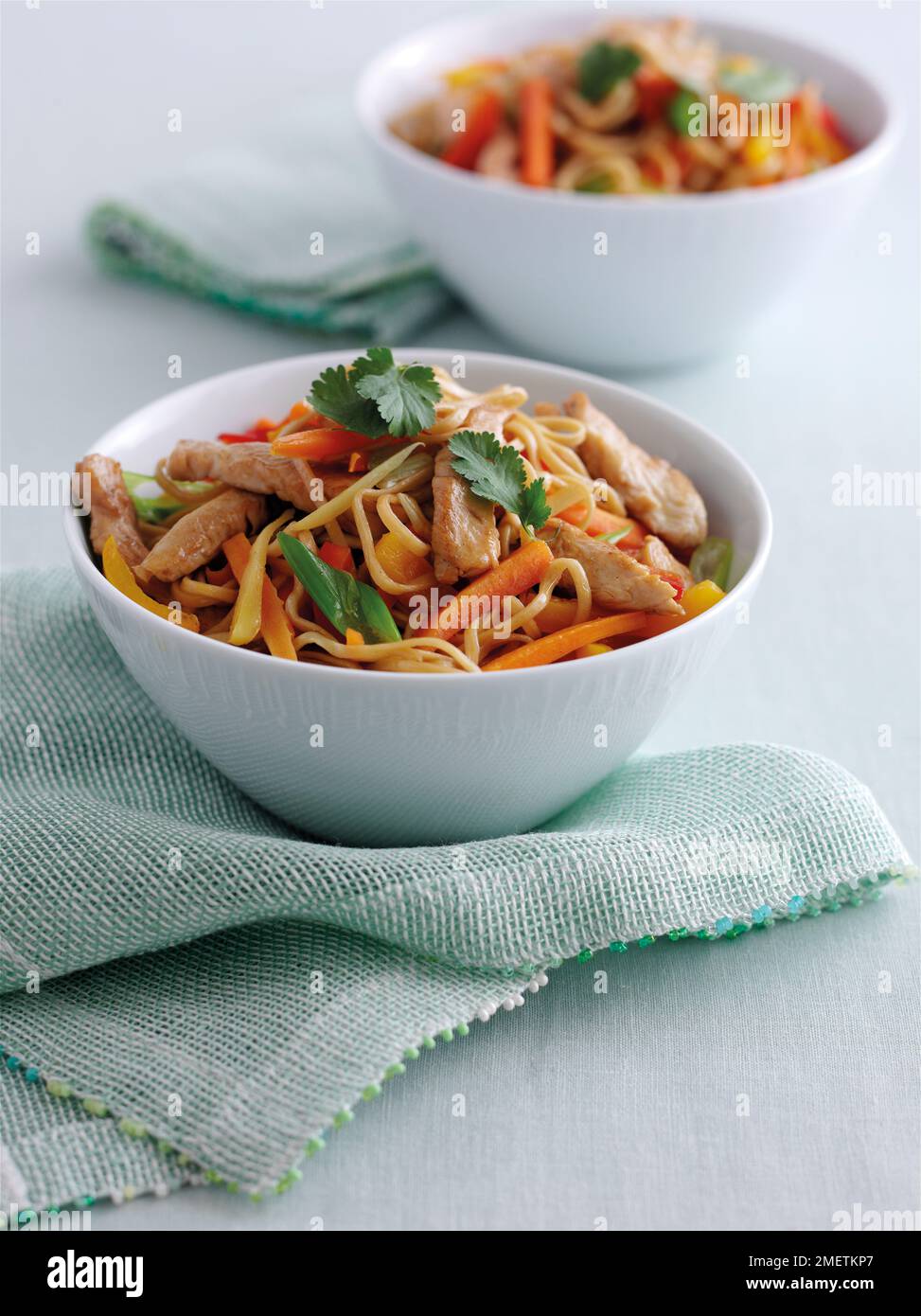 Bowls of stir-fried ginger chicken and vegetable curry served with noodles and garnished with coriander Stock Photo