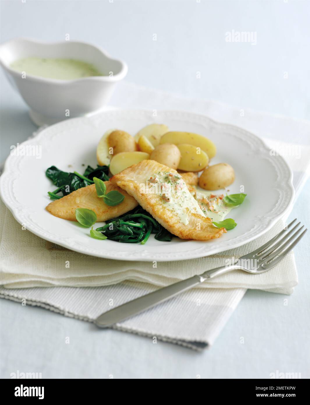 Sole fillets with creamy pesto sauce on bed of spinach, with basil leaves and boiled potatoes Stock Photo